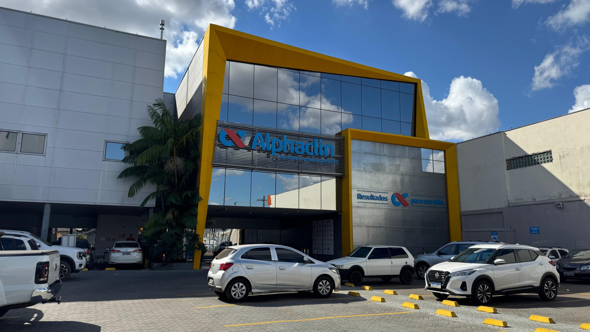 Fachada do Alphaclin Diagnósticos, com revestimento de vidro e detalhes amarelos